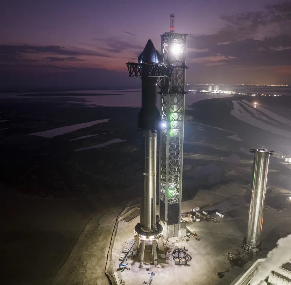 Starship e o módulo Super Heavy na plataforma de lançamento no período noturno.